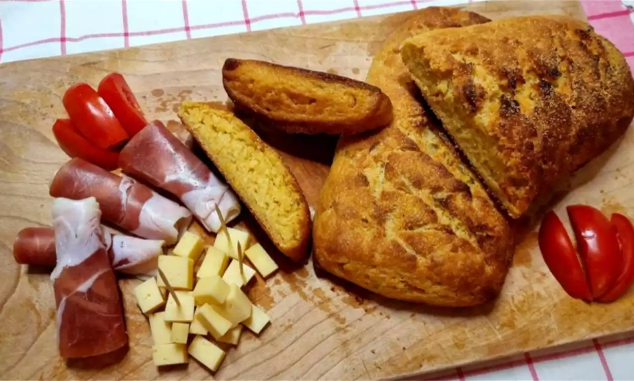 Zlatnosmeđa krušna korica sa sitnim pukotinama, deblji hrskavi sloj, komadi pršuta, sira i cherry rajčica na drvenoj podlozi