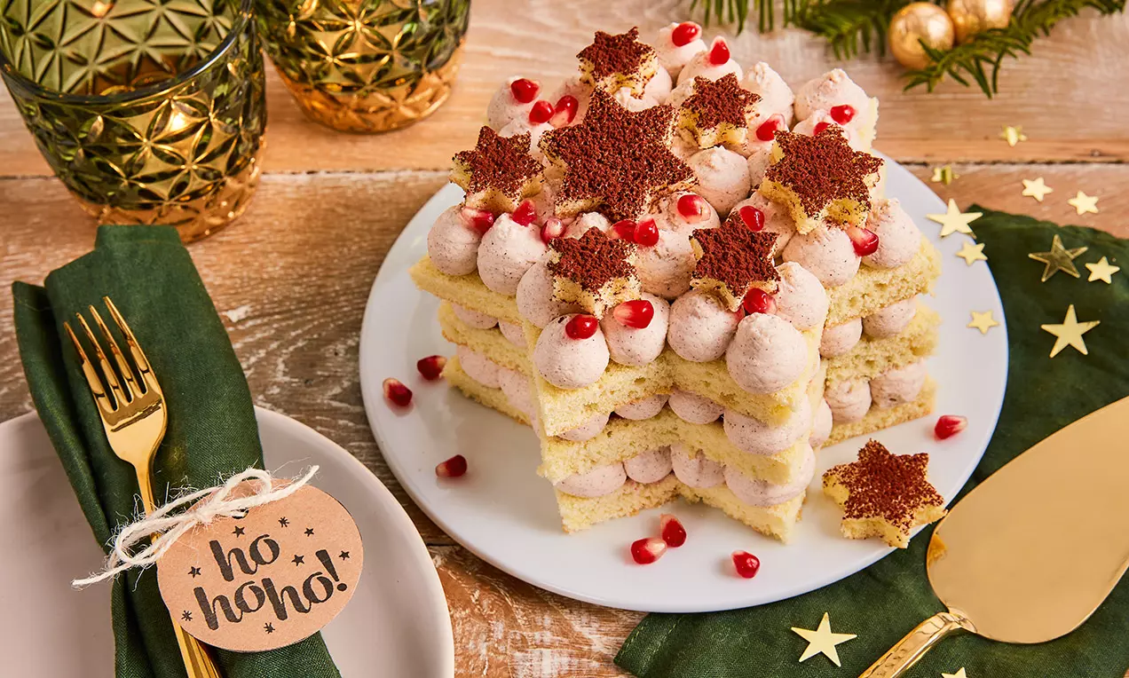 Torta u obliku zvijezde sa slojevima biskvita, kremom od cimeta, ukrašena crvenim šipkom i čokoladnim zvijezdama na bijelom tanjuru